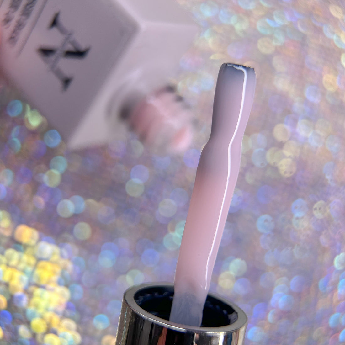 Pensel med ljusrosa rubber base färg - Bakgrunden är glittrig med en rubber base flaska som skymtar fram.