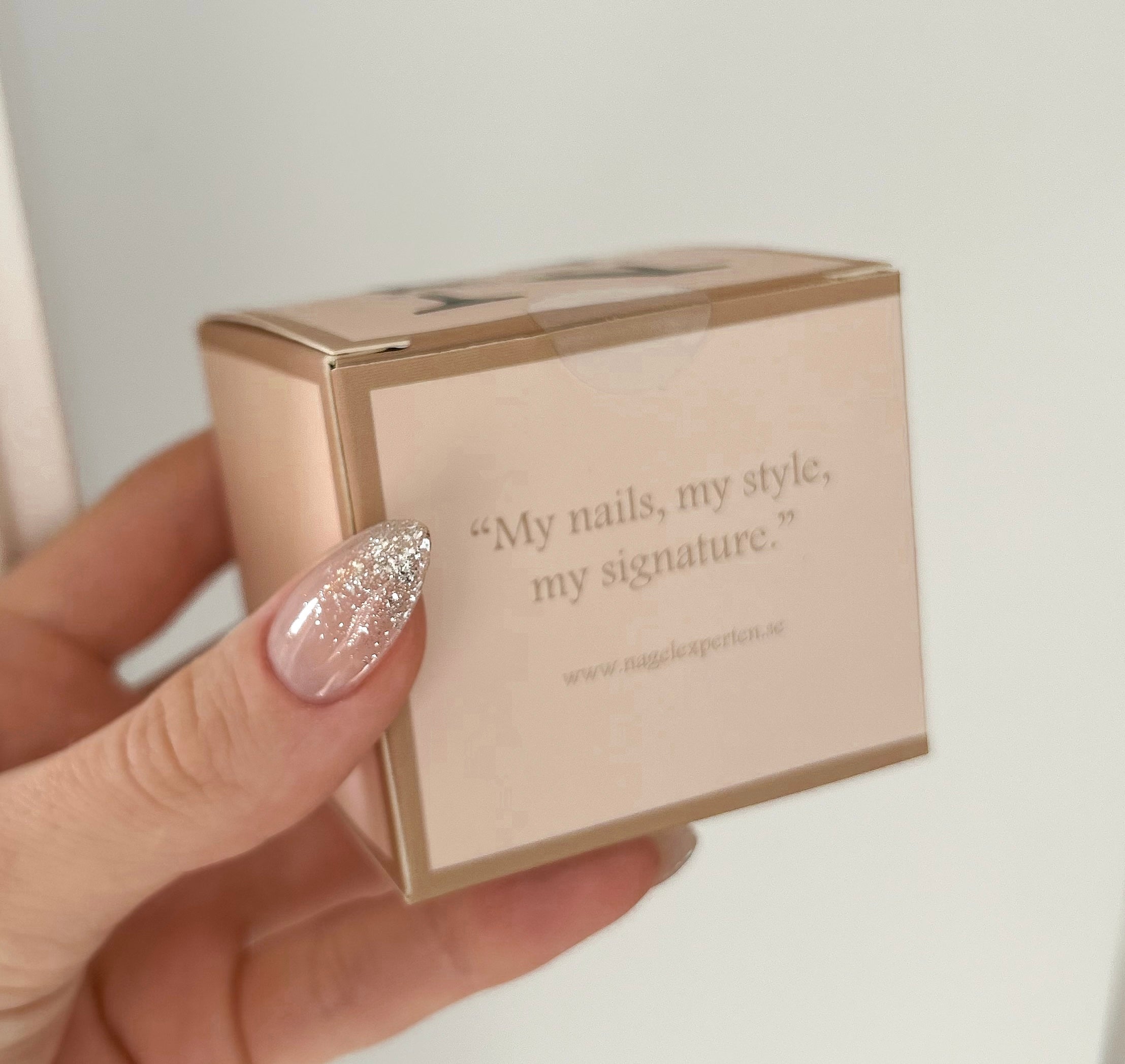 Hand med långa naglar håller i en rosa box innehållande burk med builder gel för nagelförlängning.