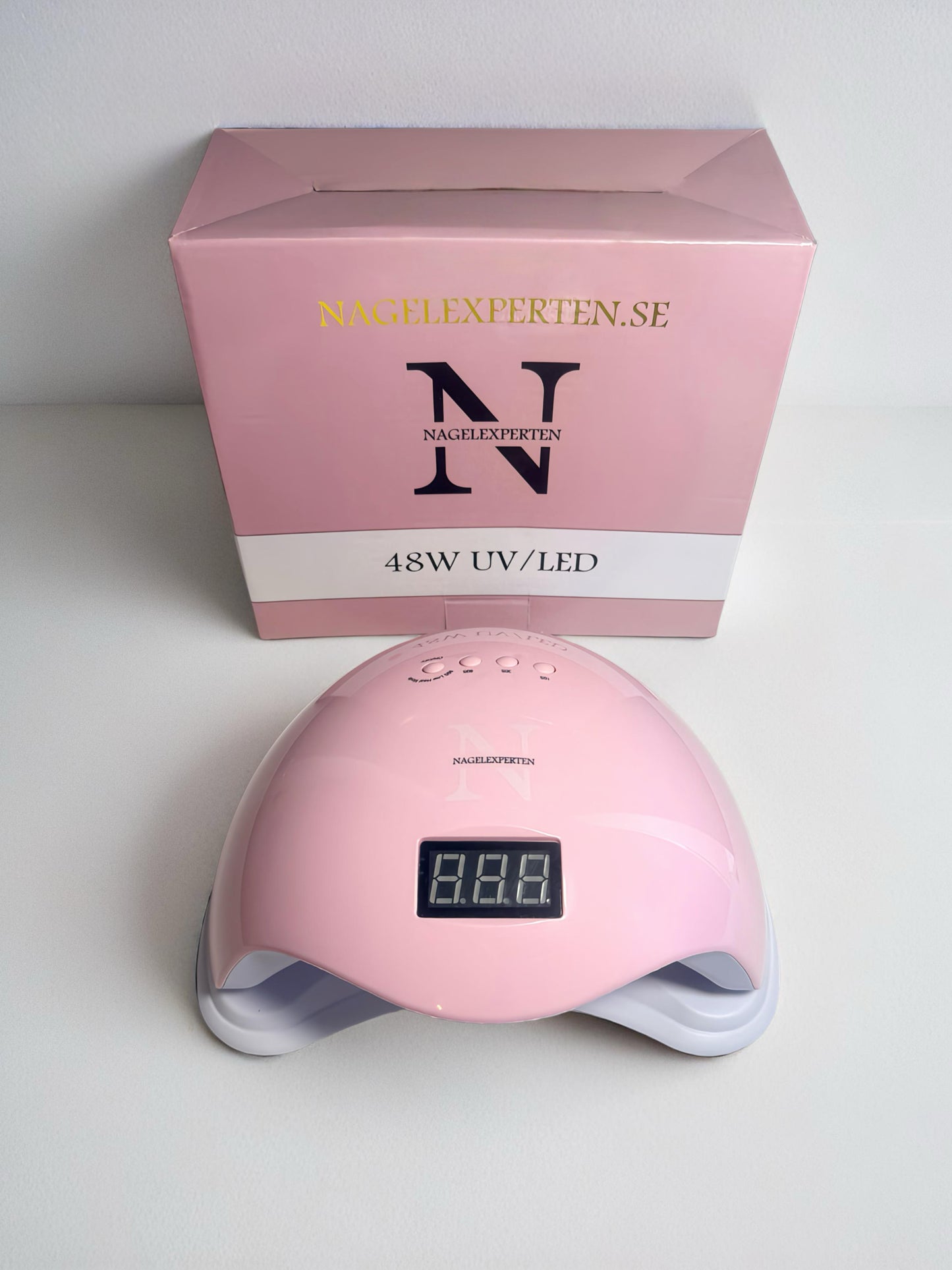 Uv led lampa för naglar i rosa färg som står på ett bord tillsammans med en rosa tillhörande kartong.