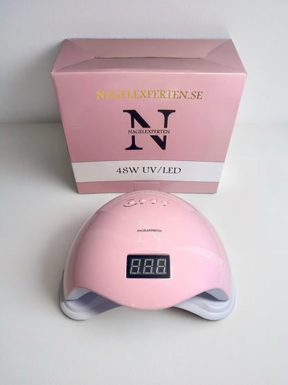 Uv led lampa för naglar i rosa färg som står på ett bord tillsammans med en rosa tillhörande kartong.